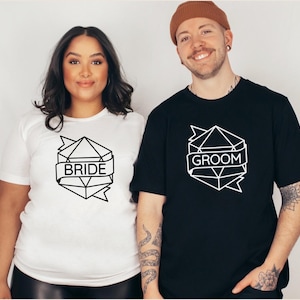 May include: A white t-shirt with the word "BRIDE" in a geometric design and a black t-shirt with the word "GROOM" in a similar design. The shirts are worn by two people, likely for a wedding or engagement.