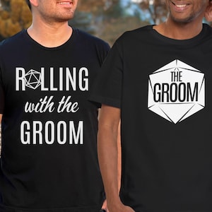 May include: Two black t-shirts with white text and a graphic of a dice. The first shirt says "Rolling with the Groom" and the second shirt says "The Groom".
