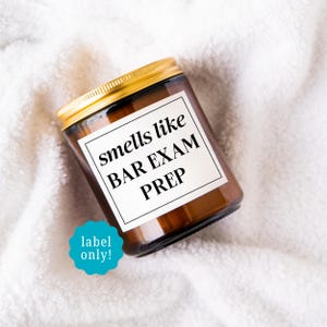 May include: A brown glass jar with a gold lid, featuring a white label that reads "smells like BAR EXAM PREP." The jar is set against a white, textured background. A teal sticker says "label only!"