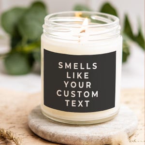 May include: A white candle in a clear glass jar with a black label that says "Smells Like Your Custom Text".