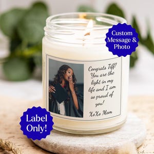 May include: A lit, white candle in a clear glass jar. The candle has a label with a photo of a woman in a graduation gown and the text "Congrats Tiff! You are the light in my life and I am so proud of you! XoXo Mom."