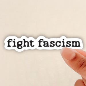 May include: White sticker with the text "fight fascism" in black typewriter font.