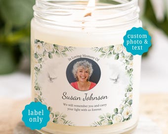 May include: A clear glass jar candle with a white wax fill and a lit wick. The label features a circular photograph of a person, the text In Loving Memory Of, Susan Johnson, and the phrase We will remember you and carry your light with us forever.