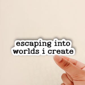 May include: White sticker with black text that reads "escaping into worlds i create"