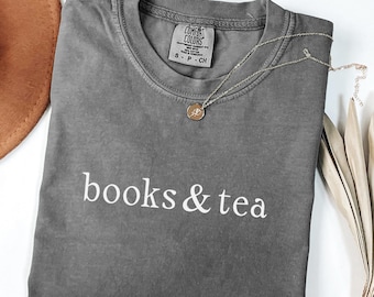 Maglietta con tema libri e tè, testo minimalista, colori comodi, regalo ideale per gli amanti dei libri e del tè.