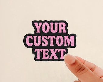 May include: A die-cut sticker featuring the words YOUR CUSTOM TEXT in a bold, sans-serif font. The lettering has a bright pink glitter finish and is outlined with a thick black border, creating a high-contrast look for this adhesive label.