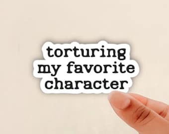 May include: A white sticker with the text "torturing my favorite character" in a black, bold font. The sticker is held by a person's fingers against a neutral background.