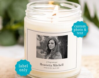 May include: A clear glass jar candle with a white wax fill and a lit wick. The label features a black and white portrait of a person, the text "In loving memory of Henrietta Mitchell", and the dates "October 06, 1952 - May 07, 2025".