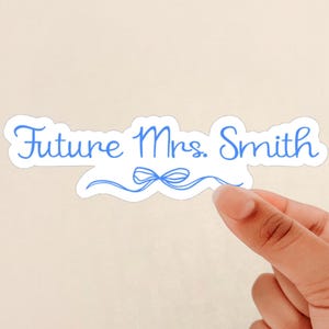 May include: A white sticker with blue text that reads "Future Mrs. Smith" with a blue ribbon underneath.