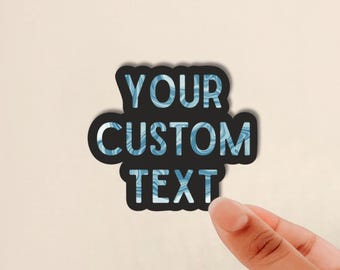 May include: A custom sticker featuring the words YOUR CUSTOM TEXT in a bold, blocky font. The letters have a light blue and white marbled pattern, and the entire text is outlined with a thick black border against a solid black background.
