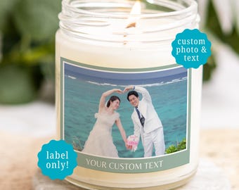 May include: A clear glass jar candle with a lit wick, featuring a custom rectangular label with a photograph of a couple in wedding attire at the beach and the text "YOUR CUSTOM TEXT". Two teal scalloped badges read "custom photo & text" and "label only!".