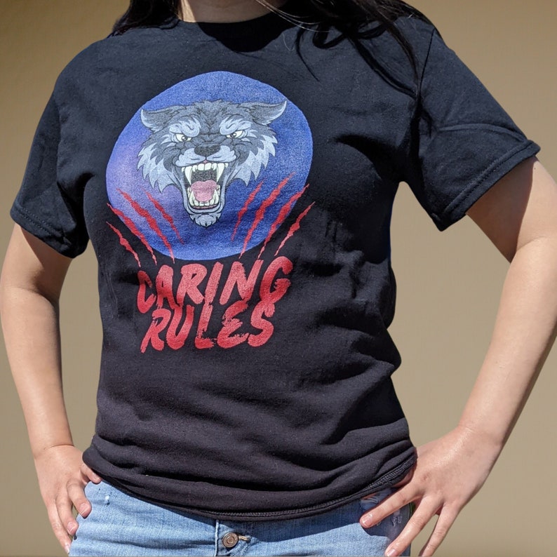 May include: Black t-shirt with a blue and red graphic of a wolf's head with claws and the text "Caring Rules".