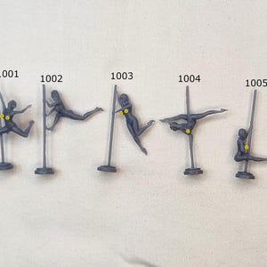 May include: A collection of miniature figurines depicting various poses of a person pole dancing. The figurines are dark gray with yellow accents and are numbered 1001 through 1009.
