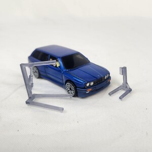 May include: A blue toy car with silver rims and a clear plastic car lift. The car lift is in two pieces. The car is a station wagon style. The background is white.