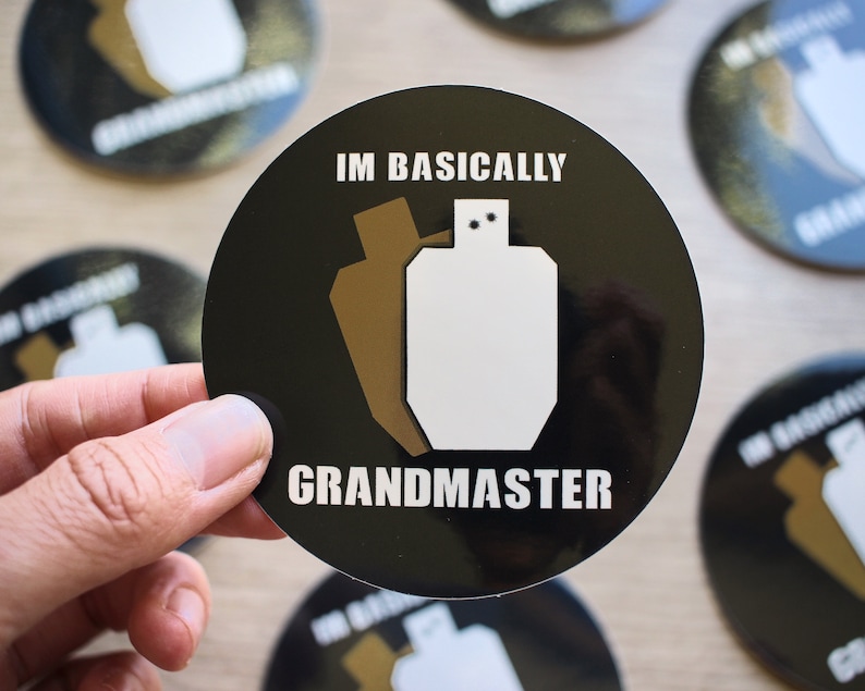 High quality glossy vinyl sticker in a circle shape with a black background. There are 2 shooting targets, one white and one brown with the words Im Basically Grandmaster. A humorous sticker for USPSA competitive shooters.