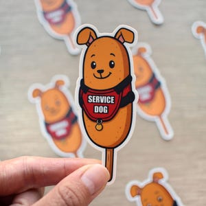 May include: A sticker featuring a cartoon dog designed as a corn dog, wearing a red vest that says "SERVICE DOG". The dog is light brown with a smiling face. Other similar stickers are scattered around.