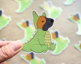 Peut inclure: Un chien vert et brun portant un costume de dinosaure. Le chien sourit et a une expression joyeuse. Le costume a une longue queue et des dents pointues.