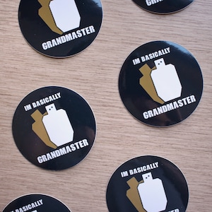 High quality glossy vinyl sticker in a circle shape with a black background. There are 2 shooting targets, one white and one brown with the words Im Basically Grandmaster. A humorous sticker for USPSA competitive shooters.