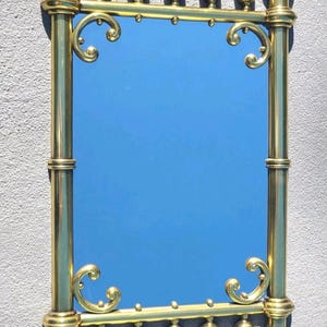 May include: A rectangular mirror with a brass frame. The frame features ornate detailing, including rounded finials and decorative scrollwork. The mirror's reflective surface is a vibrant blue, contrasting with the gold color of the frame.