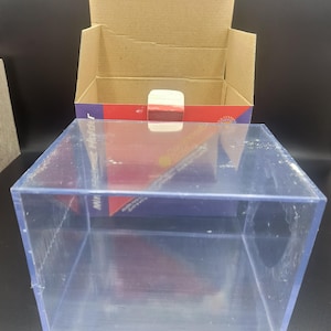 May include: A clear plastic display case with a cardboard box inside. The box is open and has a red and blue design with the words "Miniatures" and "Lasting Impressions" printed on it.