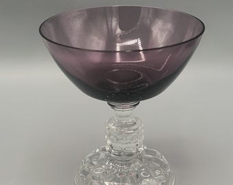 May include: A purple glass goblet with a clear glass stem and base. The base has a decorative pattern.