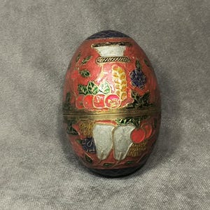 May include: A red, white, and blue egg-shaped trinket box with a floral design. The box is made of brass and has a hinged lid.