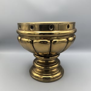 May include: A gold-colored metal bowl with a fluted design and a round base. The bowl has a decorative rim with small holes.