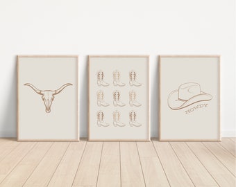 May include: Three beige framed prints with brown line drawings. The left print features a bull skull. The center print features nine cowboy boots. The right print features a cowboy hat with the word "Howdy" underneath.