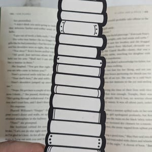May include: Black and white bookmark shaped like a stack of books. The bookmark is designed to look like a stack of books with a simple, minimalist design.