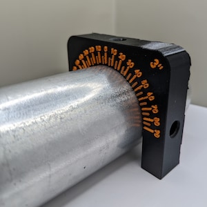 Puede incluir: Un transportador negro impreso en 3D con una escala naranja, unido a un tubo de metal plateado. El transportador está marcado con grados de 0 a 90.