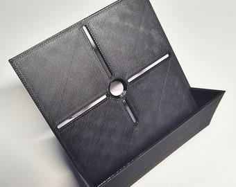 May include: A black 3D printed stand with a square base and a raised lip on one side. The base has a circular hole in the centre and four slots radiating out from the hole.