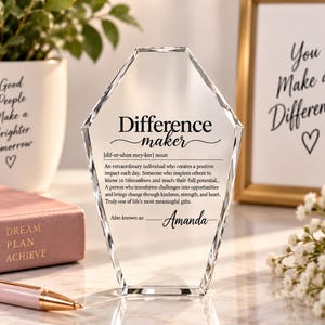 May include: A clear, faceted, diamond-shaped glass award featuring black printed text that defines the term Difference maker, including a phonetic pronunciation, a descriptive paragraph, and the personalised name Amanda at the bottom.
