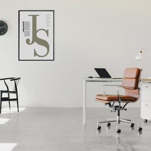 May include: A contemporary office setting featuring a white desk, a brown leather chair, and a black laptop. A framed poster with the letters "JS" and the year "1995" is on the wall. A black clock and a small plant are also present.