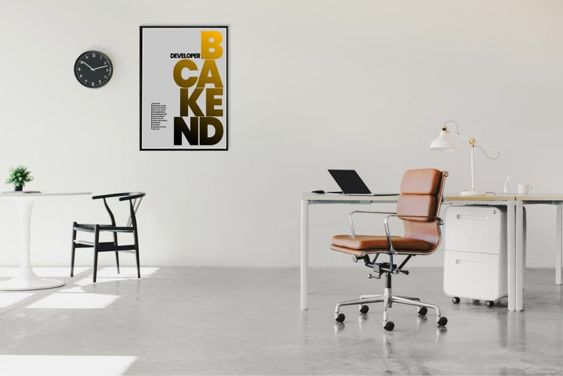 May include: An office interior with a modern aesthetic. A framed poster with the words "DEVELOPER CAKE BEND" in gold and black hangs on a white wall. A brown leather office chair sits near a desk with a laptop and lamp.