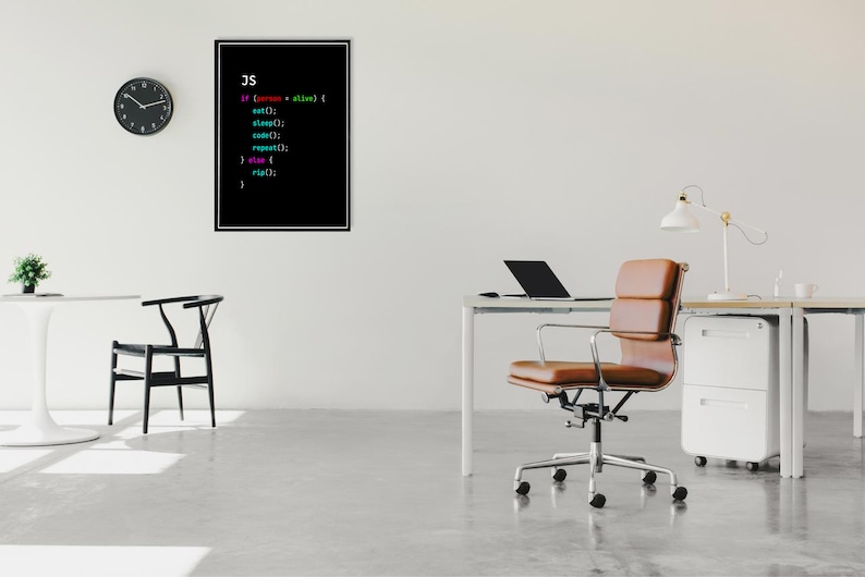 May include: A black and white framed print with the text "JS" and code in various colors. The print is hanging on a white wall in a modern office setting. A brown leather office chair is in the foreground, and a white desk with a laptop and a lamp is in the background.