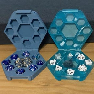 May include: Two hexagonal dice trays, one blue and one teal, with lids. The blue tray has a set of blue and gold dice inside. The teal tray has a set of white dice inside.