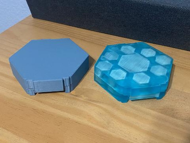 May include: Two hexagonal shaped 3D printed objects. One is a light blue color and the other is a dark blue color.