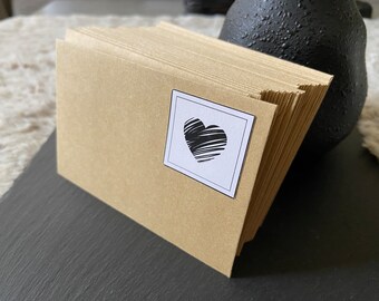 May include: A stack of brown kraft paper envelopes with a black heart sticker on the front. The sticker is in a white square frame.