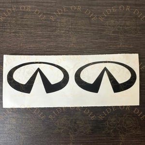 May include: Two black Infiniti logo decals on a white background. The decals are oval-shaped with a triangular design inside. The words "RIDE OR DIE" are printed in a semi-circle above the decals.