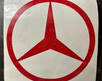 May include: A red Mercedes-Benz logo sticker. The sticker features the iconic three-pointed star within a circular frame. The sticker is on a white background with a floral pattern.