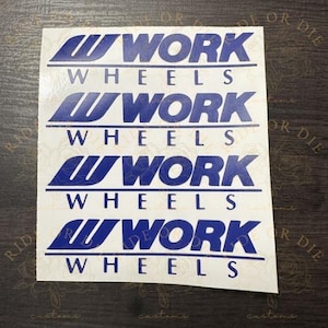 May include: A white rectangular decal sheet featuring four identical blue graphic logos. Each logo consists of a stylized W icon followed by the text WORK, with the word WHEELS printed in blue capital letters directly underneath each logo.