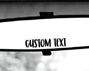 May include: A black rearview mirror with the text "CUSTOM TEXT" printed on the reflective surface.