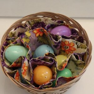 May include: A wicker basket filled with colorful Easter eggs wrapped in floral fabric. The eggs are a mix of purple, blue, green, and yellow.