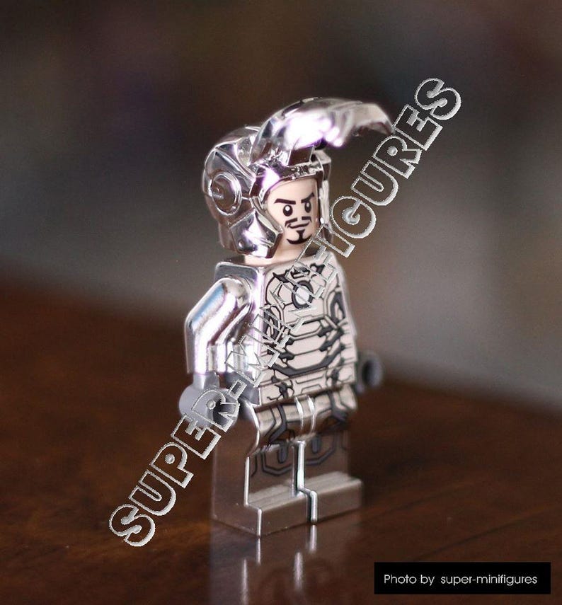 Puede incluir: Una minifigura Lego de Iron Man plateada con un traje plateado y negro y un casco plateado. La minifigura est&aacute; de pie sobre una superficie de madera.