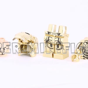 Puede incluir: Piezas de minifigura Lego doradas que incluyen un torso, piernas, cabeza y dos manos. El torso tiene un dise&ntilde;o dorado y negro. La cabeza tiene una cara dorada con un ojo negro y una boca negra. Las piernas son doradas con un dise&ntilde;o negro. Las manos son doradas.