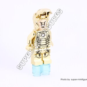 Puede incluir: Minifigura Lego dorada de Iron Man con un casco y una armadura dorados. La minifigura tiene un dise&ntilde;o negro y dorado en la armadura y una base azul transl&uacute;cida.