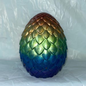 May include: A decorative dragon egg with a textured, scale-like surface. The egg transitions in color from red to gold, green, blue, and purple. The egg is an oval shape.
