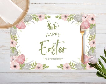 May include: White Easter placemat with floral and egg border, text "Happy Easter" and bunny ears. A gold fork and a wooden plate with napkins are on the left. A white tulip is on the right.