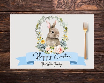 May include: Easter-themed placemat featuring a watercolor illustration of a bunny surrounded by a floral wreath. A light blue banner displays "Happy Easter" and a family name. A gold fork is placed on the right.