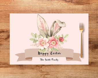 May include: A placemat with a watercolor design featuring bunny ears, pink flowers, and greenery. The words "Happy Easter" and "The Smith Family" are printed on a banner. A gold fork is placed to the right.